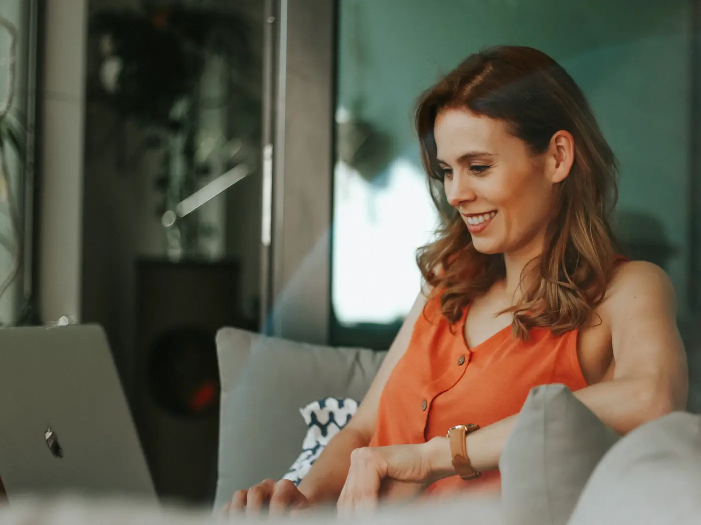 A smiling woman relaxing on her sofa, replying to messages on her laptop